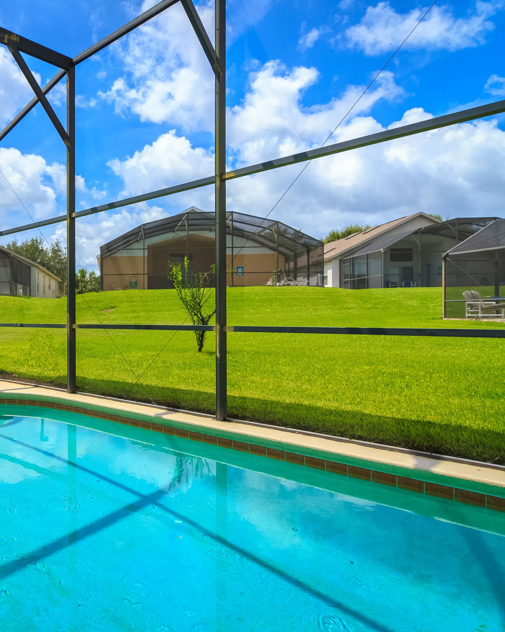 Stock photo: a backyard pool inside a screened enclosure, with neighboring screened pools and a lawn behind it under a blue sky